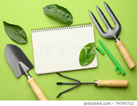 open notebook with blank white sheets and various gardening tools with wooden handles open notebook with blank white sheets and various gardening tools with wooden handles 74795722