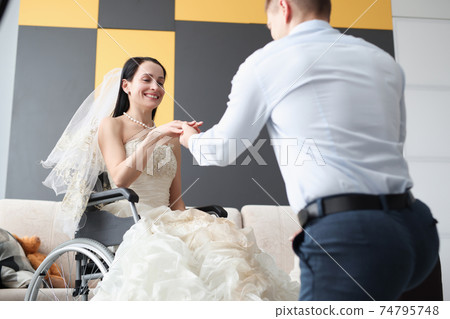 Groom putting ring on finger of bride in wheelchair 74795748
