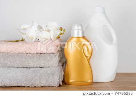 Bottles of detergent and fabric softener with clean towels and orchid flowers on wooden table. Containers of cleaning products. Liquid detergent and conditioner. Laundry day, cleaning concept. 74796253