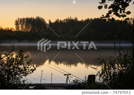 At night, two fishing rods are installed on the pier for fishing on the lake At night, two fishing rods are installed on the pier for fishing on the lake 74797051