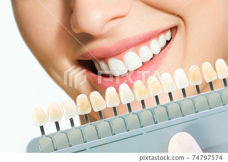 Smiling young woman. Cosmetological teeth whitening in a dental clinic. selection of the tone of the implant tooth 74797574