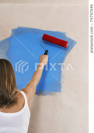 Woman Painting Wall Blue With Paint Roller 74797840
