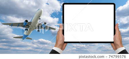 Hands with a digital tablet on the background of an airplane in the sky 74799376