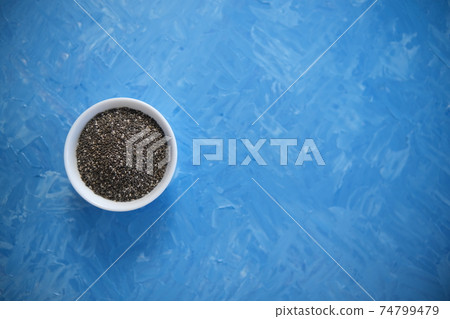 Chia seeds are organic food for a healthy diet. In a round bowl. The blue background is painted with oil paints. Chia seeds are organic food for a healthy diet. In a round bowl. The blue background is painted with oil paints. 74799479