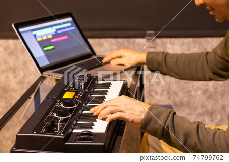 male musician enjoy playing keyboard synthesizer for arranging a song on laptop computer in home studio. music production technology 74799762