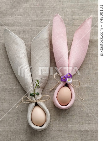 Two decorative Bunny Ears from napkin with egg on natural cotton tablecloth to Celebrate Easter Two decorative Bunny Ears from napkin with egg on natural cotton tablecloth to Celebrate Easter 74800131