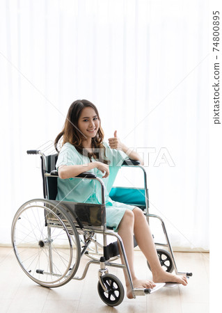 Asian patient woman sitting on wheels chair showing her thumb up. Asian patient woman sitting on wheels chair showing her thumb up. 74800895