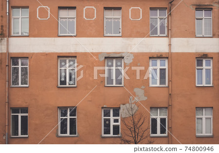 A part of yellow brown building facade with windows and a tree in front of it. Street view cityscape of Klaipeda city in Litrhuania. Retro hipster faded style of processing. Grey and gloomy mood. A part of yellow brown building facade with windows and a tree in front of it. Street view cityscape of Klaipeda city in Litrhuania. Retro hipster faded style of processing. Grey and gloomy mood. 74800946