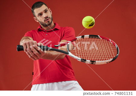 Strong sportsman in sportswear playing in tennis in the sport club isolated on red background 74801131