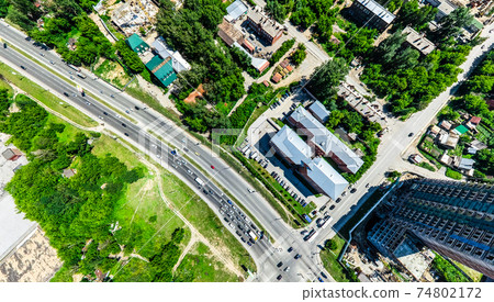 Aerial city view with crossroads and roads, houses, buildings, parks and parking lots. Sunny summer panoramic image Aerial city view with crossroads and roads, houses, buildings, parks and parking lots. Sunny summer panoramic image 74802172
