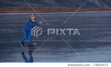 The girl train on ice speed skating. The child skates in the winter in blue sportswear suit, sport glasses. Children speed skating sport. The girl train on ice speed skating. The child skates in the winter in blue sportswear suit, sport glasses. Children speed skating sport. 74803472