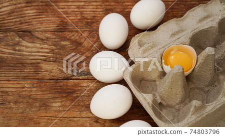 White eggs carton and cracked egg half with yolk top view on wooden background 74803796