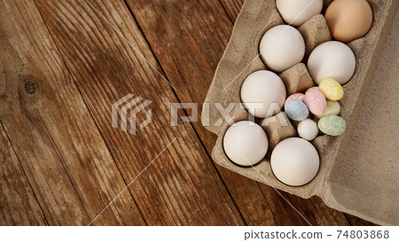 Chicken eggs in a cardboard tray and Easter decor on a wooden background. 74803868