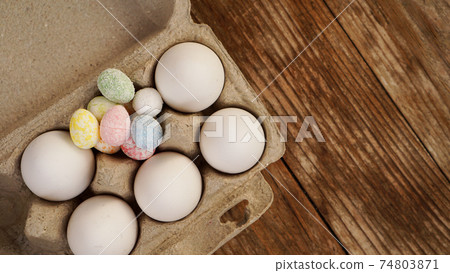 Chicken eggs in a cardboard tray and Easter decor on a wooden background. Chicken eggs in a cardboard tray and Easter decor on a wooden background. 74803871