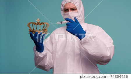 A male doctor in protective overalls and a mask makes an injection in the crown. A male doctor in protective overalls and a mask makes an injection in the crown. 74804456