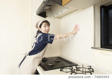 A female house cleaning worker cleaning the area around the gas stove 74805043