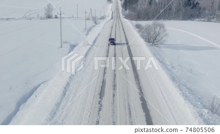 Aerial view of a red car or SUV driving along the snow covered road in winter Aerial view of a red car or SUV driving along the snow covered road in winter 74805506