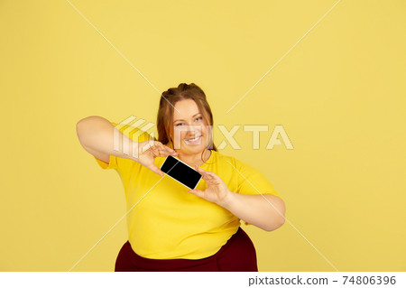 Beautiful caucasian plus size model isolated on yellow studio background. Concept of inclusion, human emotions, facial expression Beautiful caucasian plus size model isolated on yellow studio background. Concept of inclusion, human emotions, facial expression 74806396