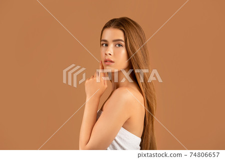 Millennial woman with long straight hair touching her face, having soft healthy skin and nude makeup on brown background Millennial woman with long straight hair touching her face, having soft healthy skin and nude makeup on brown background 74806657