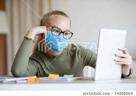 Bored teen girl in face mask using digital tablet Bored teen girl in face mask using digital tablet 74806660