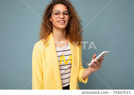 Portrait of attractive young woman with curly dark blond hair wearing yellow jacket and optical 74807615