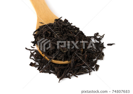 Black tea on a white background. A pile of dry tea leaves on a wooden spoon. 74807683