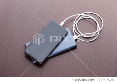 Power bank and smartphone on wooden table. The smartphone is charging from the power bank. 74807980