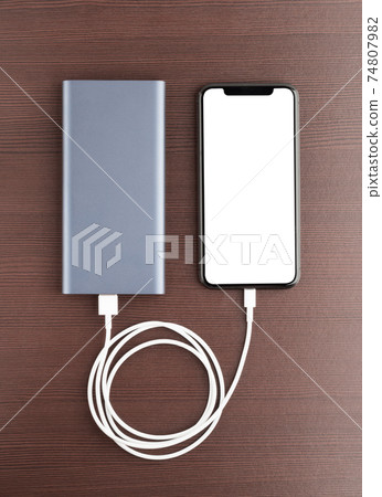 Power bank and smartphone on wooden table. The smartphone is charging from the power bank. Power bank and smartphone on wooden table. The smartphone is charging from the power bank. 74807982