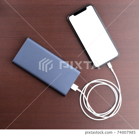 Power bank and smartphone on wooden table. The smartphone is charging from the power bank. Power bank and smartphone on wooden table. The smartphone is charging from the power bank. 74807985