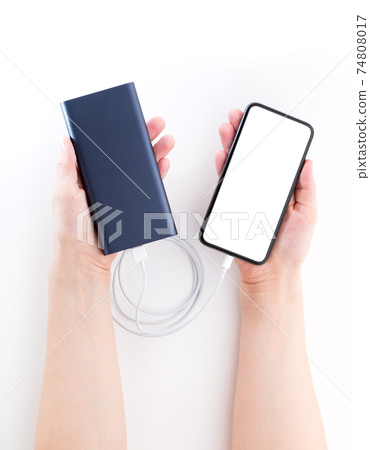 Power bank and smartphone in hands on a white background. The smartphone is charging from the power bank. Power bank and smartphone in hands on a white background. The smartphone is charging from the power bank. 74808017