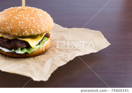 Burger on parchment paper. Beef patty burger, cheddar cheese, lettuce, bacon, tomato and balsamic sauce. Burger on parchment paper. Beef patty burger, cheddar cheese, lettuce, bacon, tomato and balsamic sauce. 74808341
