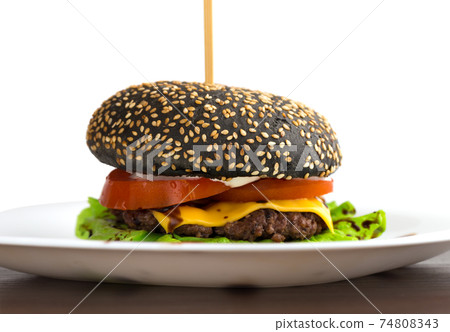 Black burger on a white plate. Beef patty burger, cheddar cheese, lettuce, bacon, tomato and balsamic sauce. The bun is made with the addition of ink cuttlefish. 74808343