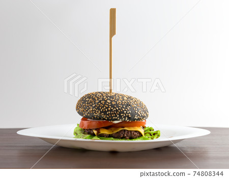 Black burger on a white plate. Beef patty burger, cheddar cheese, lettuce, bacon, tomato and balsamic sauce. The bun is made with the addition of ink cuttlefish. 74808344