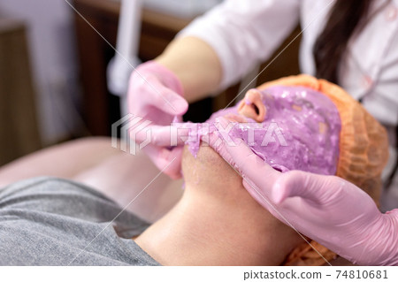 professional beautician removing purple facial mask from patient professional beautician removing purple facial mask from patient 74810681