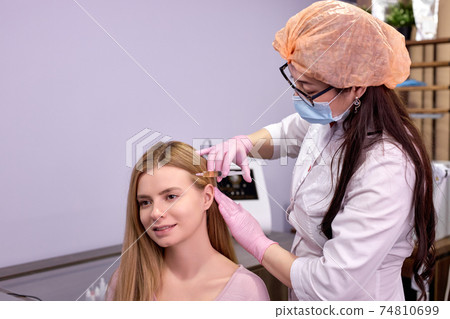 caucasian woman at trichologist office get injections in head skin by professional 74810699