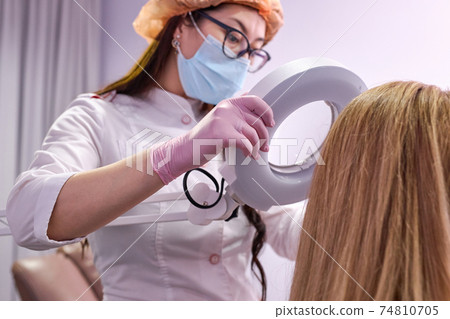 female dermatologist looking at a dermatoscope while examining female head and hair female dermatologist looking at a dermatoscope while examining female head and hair 74810705