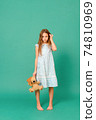 sad white teenage girl 10 years old in a blue dress holding a toy bear on a green 74810969