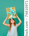 teenage girl holding a blue dress holds a gift box over her head on a green background 74810971