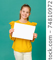 teenage girl 10 years old in a yellow blouse holding a white sign and smiling on a green background 74810972