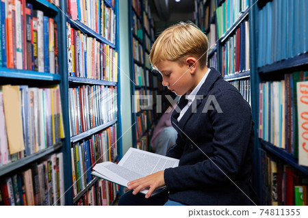 adorable little caucasian boy is sitting in a book store and read book adorable little caucasian boy is sitting in a book store and read book 74811355