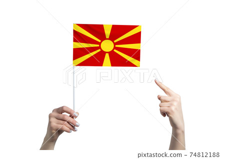 A beautiful female hand holds a Northern Macedonia flag to which she shows the finger of her other hand, isolated on white background 74812188