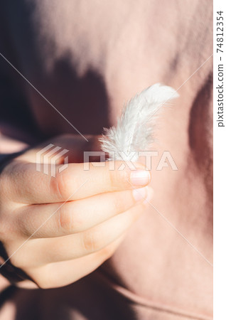 Light white feather in young girl hands Light white feather in young girl hands 74812354