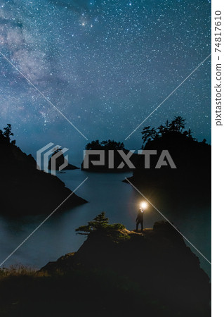 Secret Beach Oregon at Night with Stars and hiker Standing with the Light 74817610