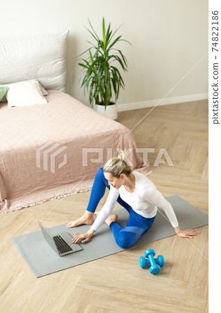 Adult caucasian woman sit on the floor in front of a laptop and set up a video call with fitness trainer to do some online workout at home, vertical photo, selective focus. Adult caucasian woman sit on the floor in front of a laptop and set up a video call with fitness trainer to do some online workout at home, vertical photo, selective focus. 74822186