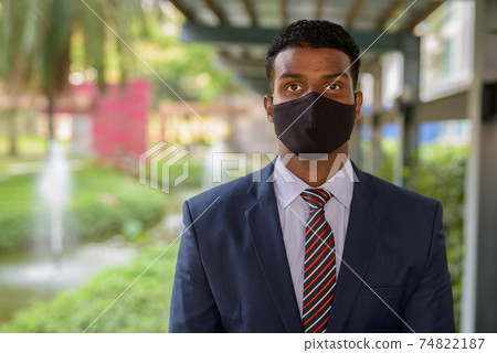 Confident African businessman with face mask for protection outdoors looking at camera Confident African businessman with face mask for protection outdoors looking at camera 74822187