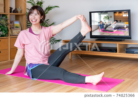 Online yoga young woman stretching in the living room 74825366