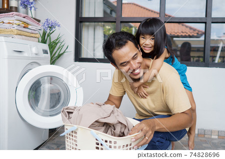 father playing piggy back ride together with daughter while doing laundry 74828696