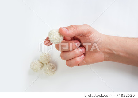 Male hand holds white chocolate candy on white background. Handmade candies, Sweet balls. Isolated background. Selective focus. Male hand holds white chocolate candy on white background. Handmade candies, Sweet balls. Isolated background. Selective focus. 74832529