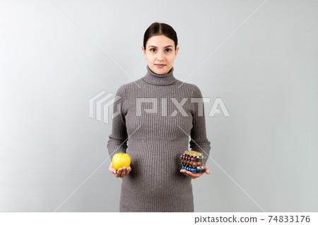 pregnant woman making a choice between an apple and a pile of pills at colorful background with copy space. Taking vitamins during pregnancy concept 74833176