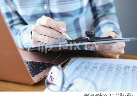 Manager sits at his desk and holds documents with pen 74833295